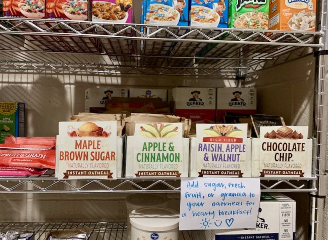 Oatmeal is one of the most popular items in The Shop. Oatmeal boxes on the shelf with a card saying add sugar, fresh fruit, or granola to your oatmeal for a hearty breakfast!