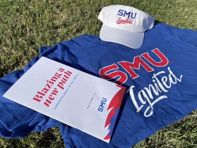 A blue shirt, white cap, and white brochure arranged on a green lawn
