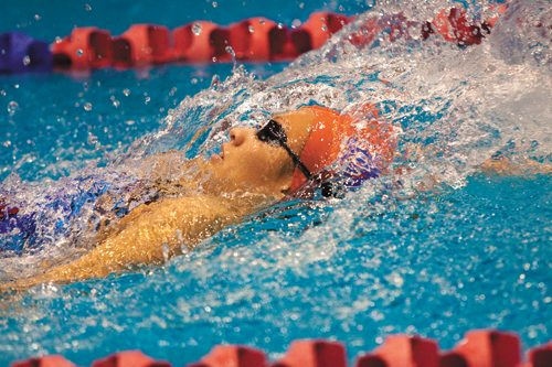 Top, A member of the women’s swimming team backstrokes during a competition.