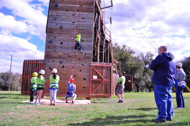 Children and parents watch as campers climb to the top of the ropes course