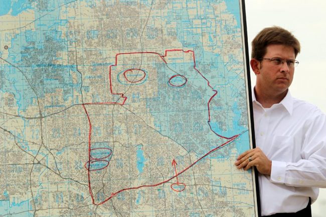 An operations manager at Dallas Executive Airport helps hold up a map of Dallas County that highlights areas targeted for spraying.