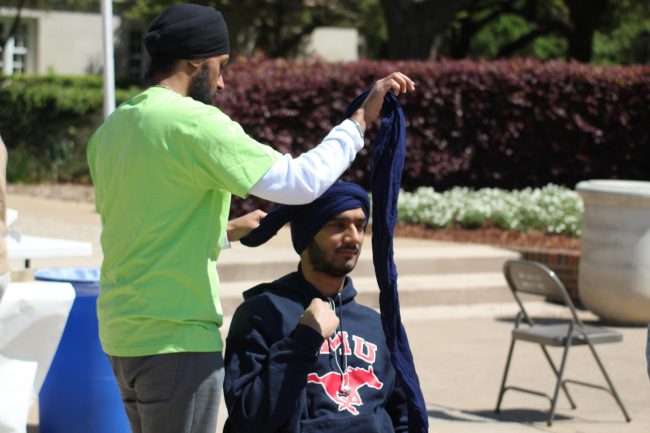 SMU Sikh Students Association President Parminder Deo ties a turban around student Alli Schloeman.