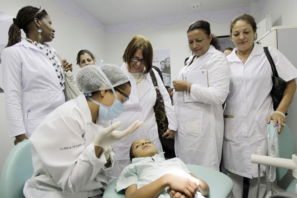 Cuban doctors observe a dental procedure during a a training session at a health clinic in Brasilia, Brazil, Friday, Aug. 30, 2013. Brazil imported thousands of Cuban doctors to work in areas where medical services and physicians are scarce. The newly hired doctors will spend their first three weeks in the country studying Brazil's public health system and learning to speak Portuguese. (AP Photo/Eraldo Peres)