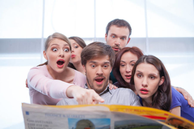 Group of young people reading newspaper. Looking very surprised and interested in