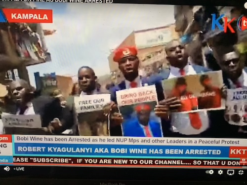 This picture is a screen capture of a YouTube video providing live coverage of protests in Uganda.  Men are marching and holding signs.