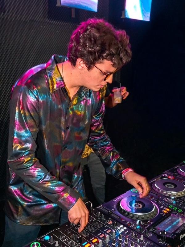 Man in a multicolored shirt DJ'ing in a dark room