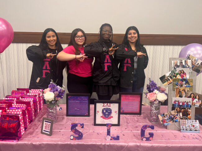 Members of Sigma Lambda Gamma, the first sorority at SMU to explicitly accept non-binary persons, pose with their sororitys hand sign in front of their booth at the Multicultural Greek Open House. Photo credit: Ceara Johnson