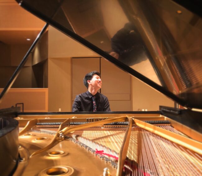 SMU student Jihoon Choi sits and grins behind a grand piano.