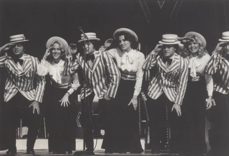 Seven female students dance on stage while the Mustang Band plays behind them in the 1970 Pigskin Revue. Courtesy of SMU Libraries.