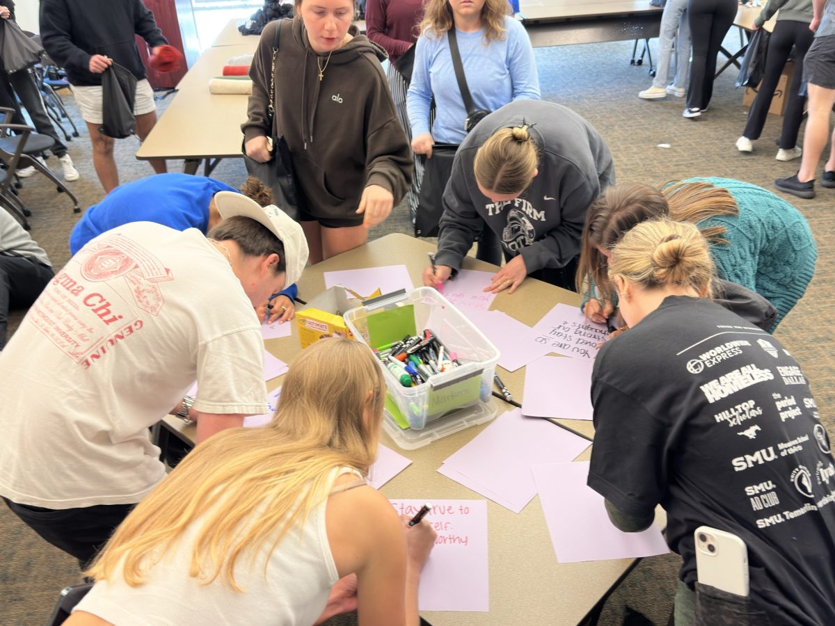 SMU students gather around a bucket of markers to write an encouraging note to put in “Welcome to the Shelter” kits at event in mid-April on SMU’s campus.