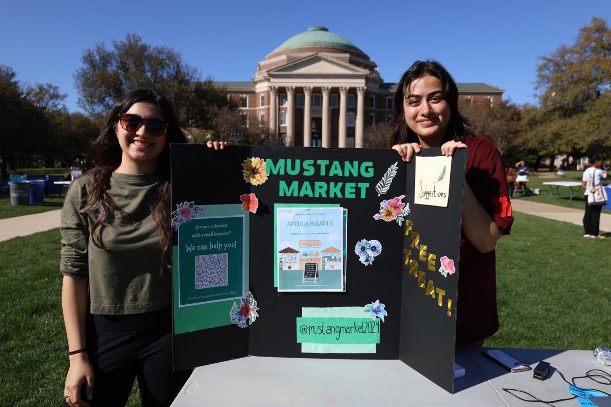 Board members of the Mustang Market hold up a sign about their event on Dallas Hall Lawn.