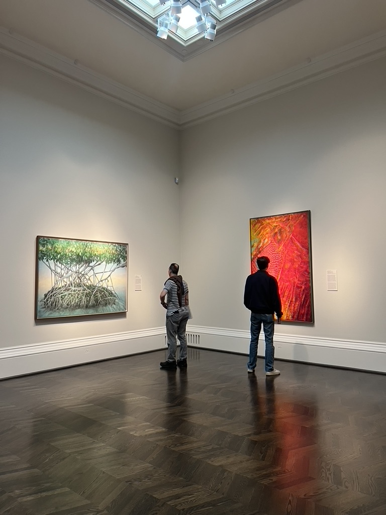 Patrons observing the first room in “The Sense of Beauty Exhibition,” displaying contrast in color scheme and featuring “El Mangle” by Myrna Báez.