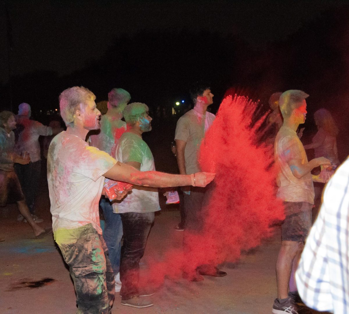 A man creates a wave of color as he throws red powder towards a group of students. The powder is called gulal, and is used to celebrate the triumph of good over evil, according to CNN.